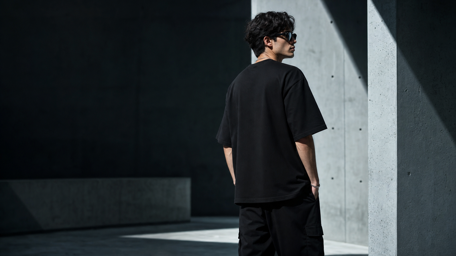 Male model wearing a plain black oversized T-shirt in a concrete editorial setting